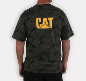 A person is wearing the CAT Trademark Tee, a dark camouflage T-shirt made from 100% cotton, with the iconic yellow "CAT" logo on the back. The casual tee contrasts with a plain, light-colored background.