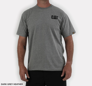 A person dons the casual CAT Trademark Tee in dark grey heather, featuring the classic "CAT" print on the upper left chest. This 100% cotton shirt, paired with black pants, stands out sleekly against a plain white background.