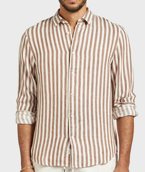 A person is wearing the Academy Brand Farrelly Linen Shirt, featuring vertically striped button-up design with alternating brown and white stripes. Made from 100% Linen, this stylish and comfortable shirt has a collar and sleeves rolled up to the forearms. Only the upper body is visible against a white background.