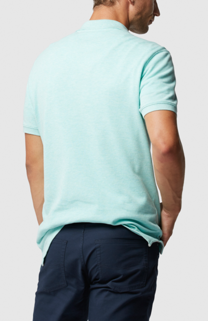 A person wearing the Rodd & Gunn The Gunn Polo in light blue, made from Australian Cotton, and navy pants stands with their hands in pockets against a plain gray background.