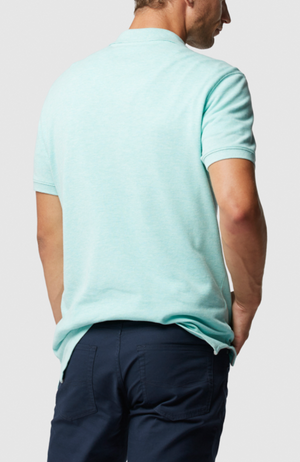 A person wearing the Rodd & Gunn The Gunn Polo in light blue, made from Australian Cotton, and navy pants stands with their hands in pockets against a plain gray background.