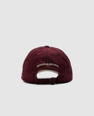 The maroon Rodd & Gunn Gunn Cap, with "RODD & GUNN" in white embroidery on the back, is crafted from heavy-duty cotton twill. An adjustable strap ensures a perfect fit, and its classic design stands out against a plain gray background.