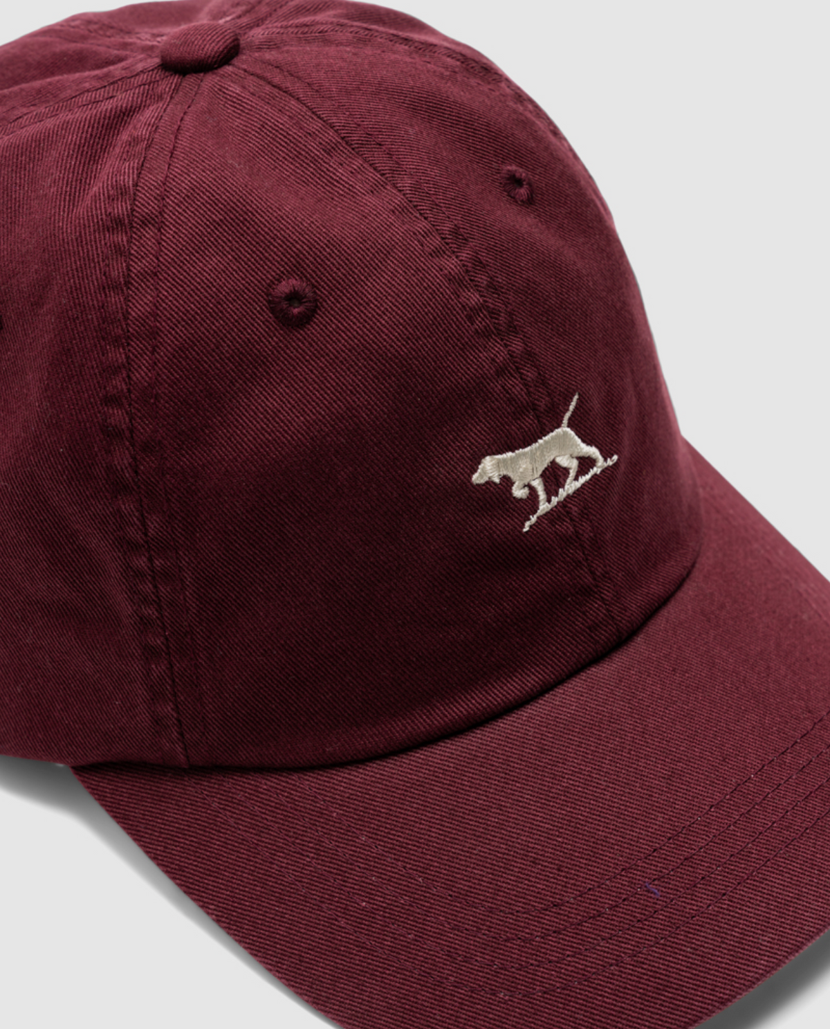 A maroon Rodd & Gunn Gunn Cap made of durable cotton twill with a white embroidered dog on the front against a plain backdrop.