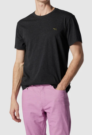 Wearing a Rodd & Gunn The Gunn T-Shirt in black, crafted from soft Australian cotton with a subtle chest emblem, and light purple pants, a person stands against a neutral background with one hand in their pocket. Their face is not visible.
