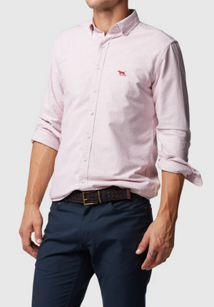 A person wears a Rodd & Gunn Oxford Stripe Sports Fit Shirt in light pink with thin stripes and a small red logo, made from 100% cotton. The long sleeves are rolled up to the forearms, paired with dark blue trousers and a woven black belt.