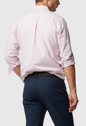 With their back to the camera, a person wears a light pink Rodd & Gunn Oxford Stripe Sports Fit Shirt made from 100% cotton. The sleeves are rolled up, paired with dark blue pants, and their left hand rests in the pocket, highlighting a stylish patterned belt.