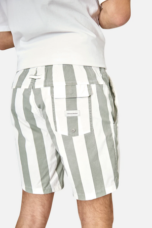 A person is wearing Industrie The Beverly Bahama Short in green and white stripes with an elastic waist and pockets, paired with a white T-shirt featuring the Industrie logo.