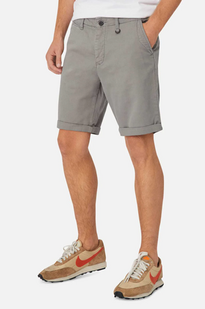A person in Industrie The Rinse Drifter Short, a black belt, and brown sneakers with orange swooshes. Their hands rest in the shorts' pockets against a plain white background.