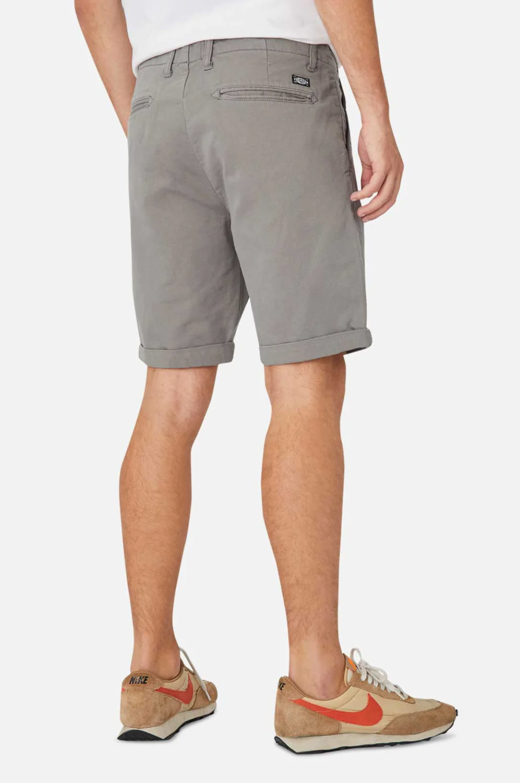 Wearing Industrie The Rinse Drifter Short and beige sneakers with orange accents, a person stands against a plain background, showcasing the relaxed fit of their shorts and shoes for a casual style.