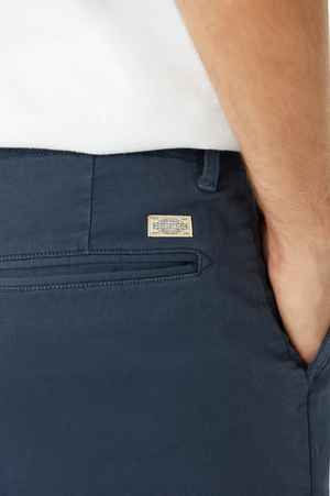 A person wears the Industrie The Rinse Drifter Short in navy, with a relaxed fit and a small label near the pocket. They're also wearing a white cotton elastane shirt.