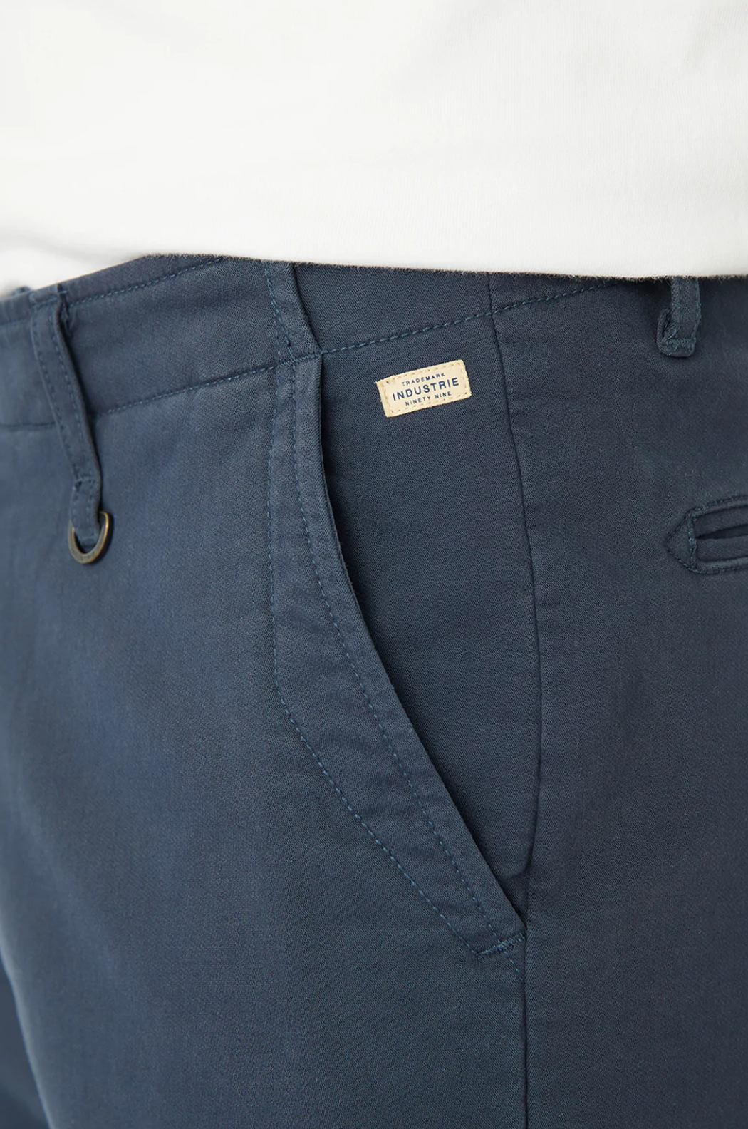 Close-up of a person wearing navy Industrie The Rinse Drifter Shorts, featuring a small "Industrie" tag near the pocket. The relaxed fit and cotton elastane blend add texture. Complete with belt loops and a button, the shorts are paired with a crisp white top.