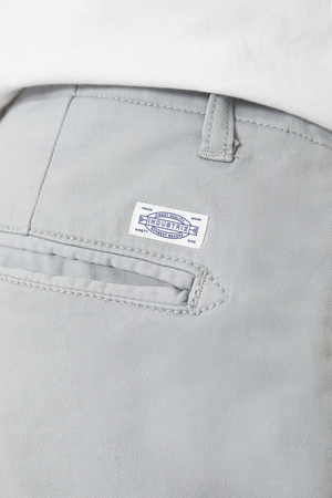Close-up of light gray Industrie The Rinse Drifter Shorts with a small white label and blue text above the back pocket, worn by someone whose white shirt is partly visible at the top.