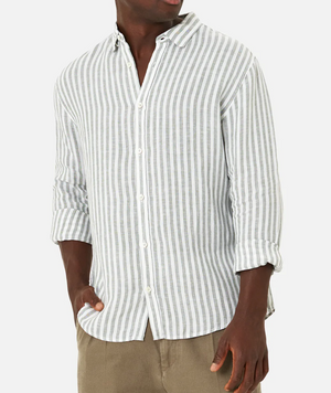 A person wears the Industrie The Bayshore Linen Shirt, a comfortable 100% linen light gray and white vertically striped button-down with rolled-up sleeves, paired with khaki pants against a plain white background, hands in pockets.