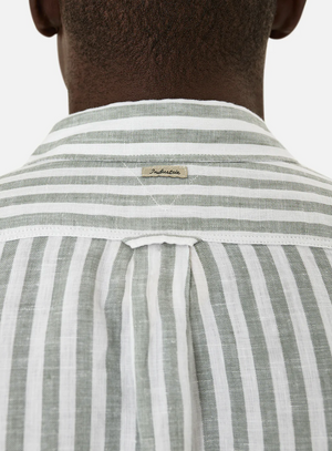 Rear view of a person wearing a comfortable gray and white vertically striped shirt, focusing on the collar tag. This stylish piece, made from 100% linen and named "Industrie The Bayshore Linen Shirt," is set against a plain, light background.