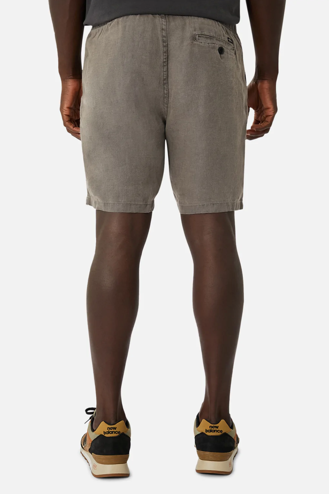 Rear view of a person in Industrie The Marina Linen Short, 100% linen gray shorts with an elastic drawstring waist and a buttoned back right pocket, paired with sneakers featuring black and tan details. White background.