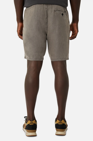 Rear view of a person in Industrie The Marina Linen Short, 100% linen gray shorts with an elastic drawstring waist and a buttoned back right pocket, paired with sneakers featuring black and tan details. White background.
