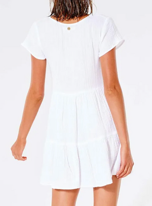 Rear view of a person wearing the Rip Curl Premium Surf Dress, featuring a short, white, textured design with short sleeves. This comfortable dress has a loose, flowing fit set against a plain white background.