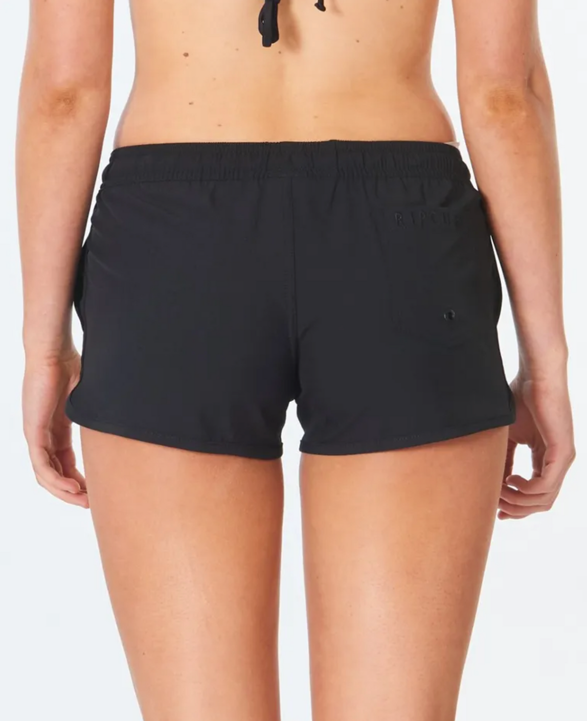 A person is seen from behind wearing Rip Curl Classic Surf 3 Boardshorts against a plain white backdrop. These black athletic shorts, made partly from recycled plastic bottles, feature an elastic waistband and a small left-side pocket, paired with a halter neck top.