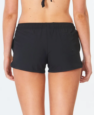 A person is seen from behind wearing Rip Curl Classic Surf 3 Boardshorts against a plain white backdrop. These black athletic shorts, made partly from recycled plastic bottles, feature an elastic waistband and a small left-side pocket, paired with a halter neck top.