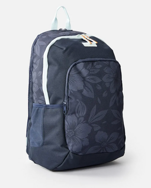 The Rip Curl Heat Wave Ozone 30L Backpack, in dark blue recycled polyester, flaunts a floral pattern of large flowers and leaves. It includes a small front zipper pocket and side mesh pocket, with the top handle and zippers highlighted by light blue accents for added style and functionality.