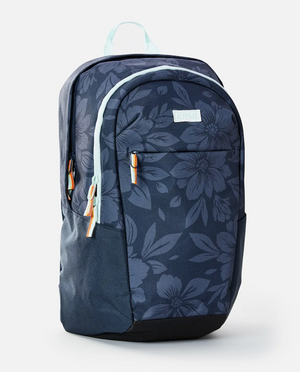 The Rip Curl Overtime 30L Backpack is made from recycled polyester, featuring a dark blue design with a large floral pattern, two main compartments suitable for a 15" laptop, light blue zippers with brown pulls, and a matching top handle on a plain white background.