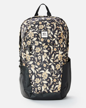 The Rip Curl Overtime 30L Backpack showcases a floral design with beige and light brown flowers on black. Made from recycled polyester, it includes side pockets, a front logo patch, and can hold a 15" laptop, offering everyday convenience.