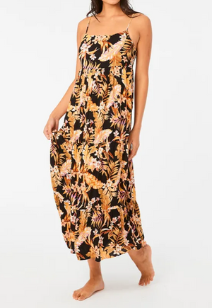 Barefoot on a neutral background, a person wears the Rip Curl Sunday Swella Midi Dress, a sleeveless black maxi crafted from EcoVero fabric with orange and pink floral patterns.