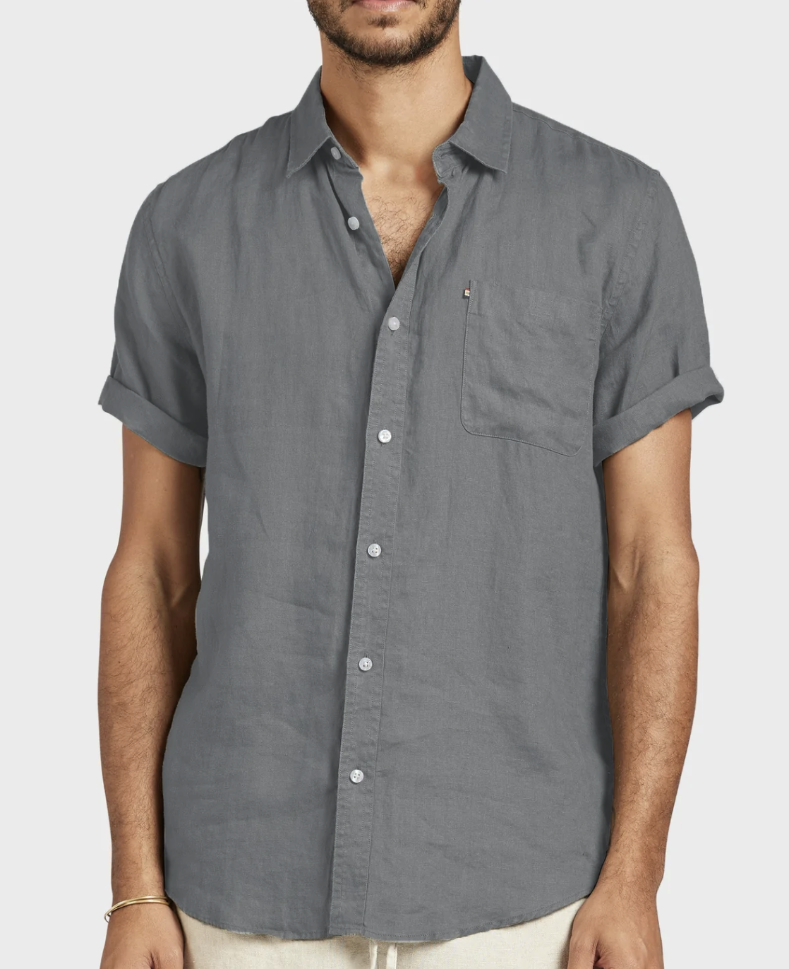 A man wears the Academy Brand Hampton Linen Short Sleeve Shirt in charcoal gray, featuring rolled cuffs and a single chest pocket, against a plain light background.