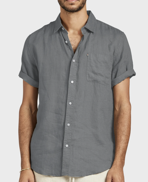 A man wears the Academy Brand Hampton Linen Short Sleeve Shirt in charcoal gray, featuring rolled cuffs and a single chest pocket, against a plain light background.