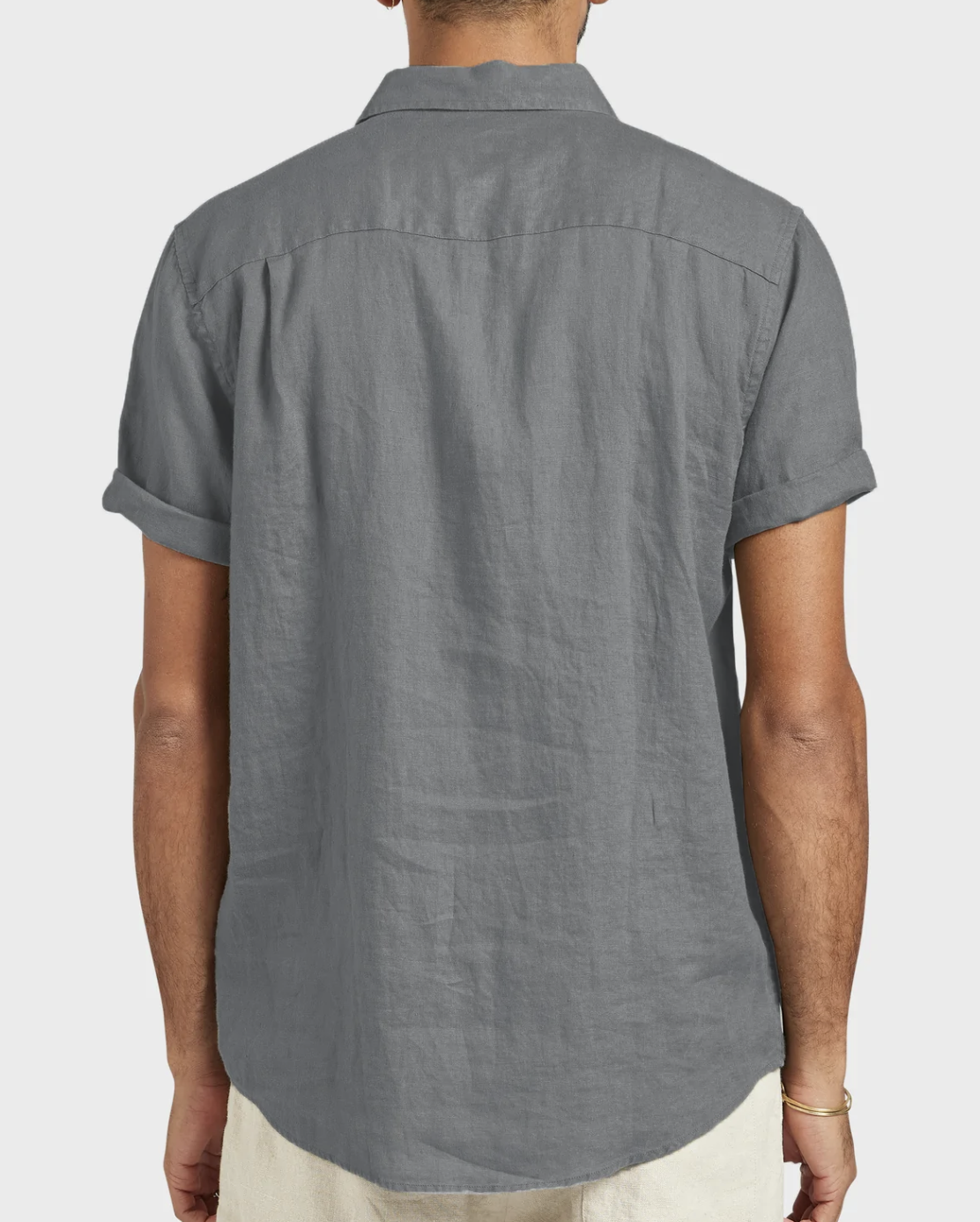 A person is seen from the back wearing the Academy Brand Hampton Linen Short Sleeve Shirt in gray, featuring rolled cuffs, paired with light-colored pants against a plain light background.