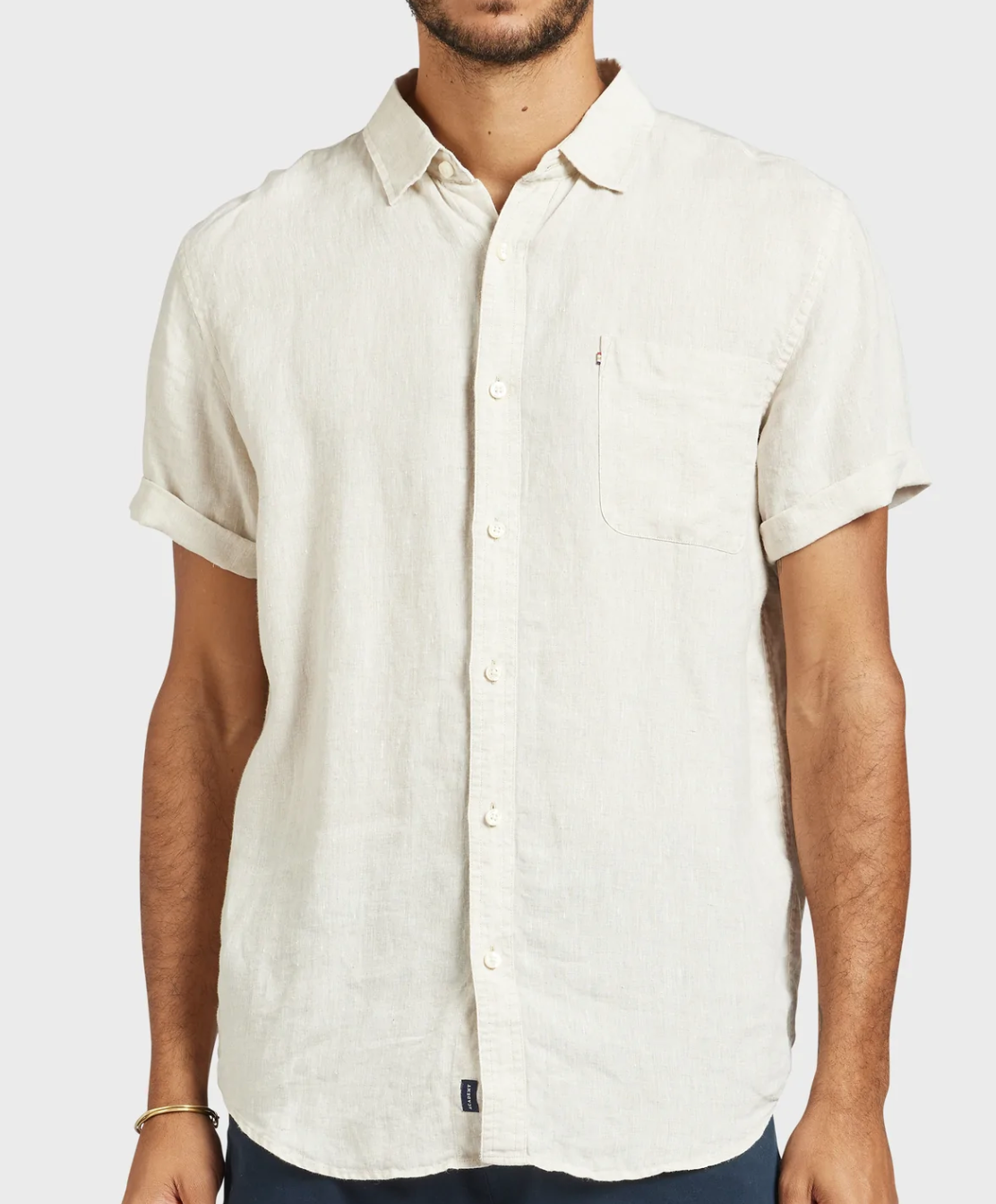 A man wears the Academy Brand Hampton Linen Short Sleeve Shirt in regular fit, off-white, featuring a left chest pocket. He stands against a plain light background with his head out of frame.