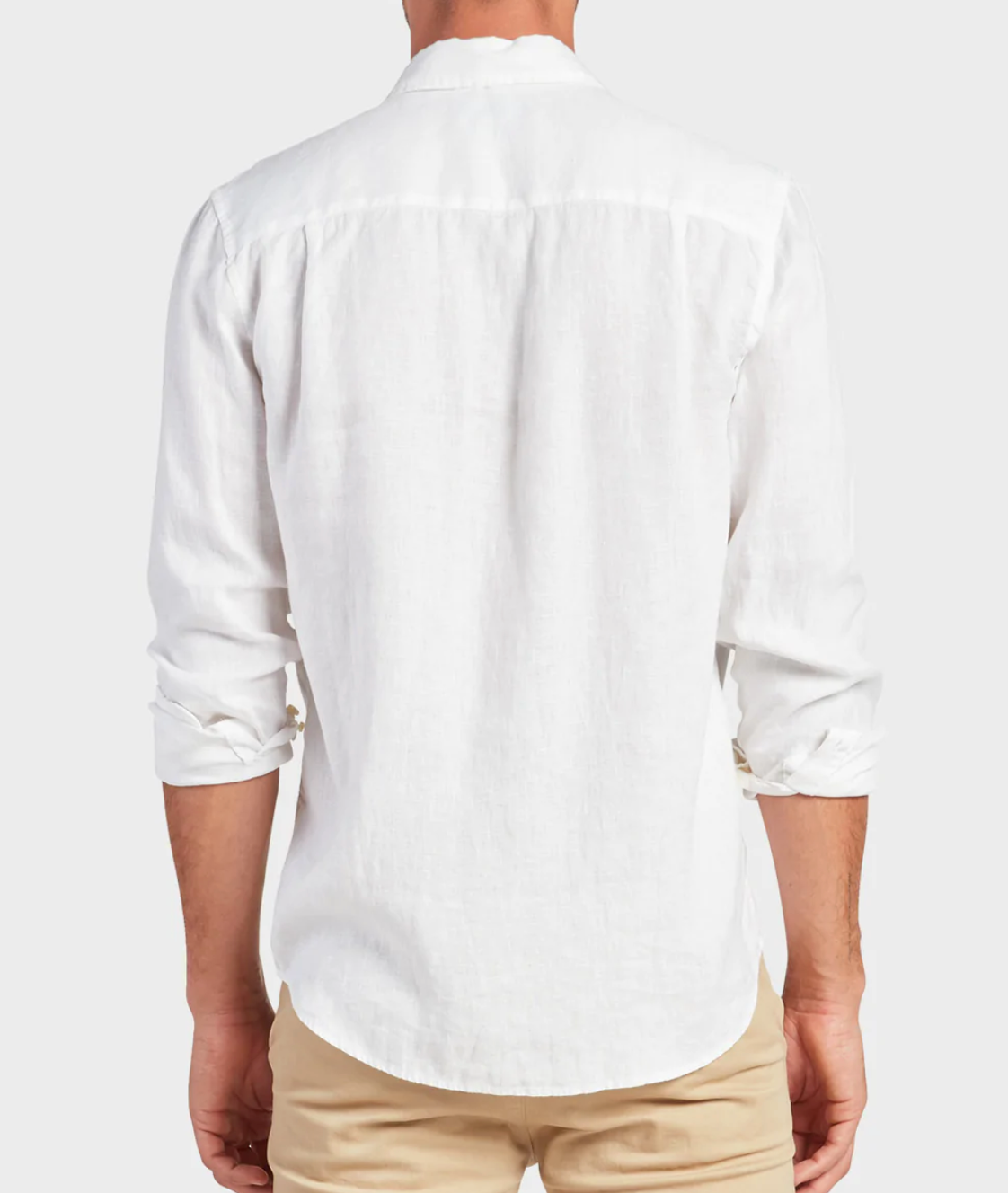 A person is seen from behind wearing an Academy Brand Hampton Linen Shirt, white and regular fit, with rolled-up sleeves. It's paired with beige pants against a light-colored, plain background.