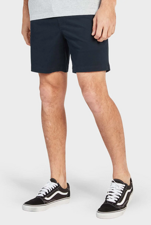 A person in a gray shirt and Academy Brand Volley Shorts, casual navy with an elastic waistband, paired with black sneakers featuring white laces, stands with hands at their sides against a plain white background.