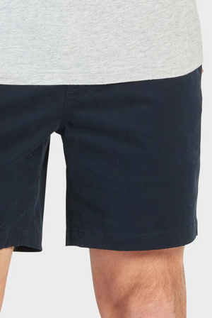 A person is wearing Academy Brand Volley Shorts in navy blue with an elastic waist, paired with a light gray shirt. Only their lower torso and legs are visible against a plain white background.