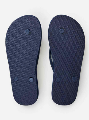 The image shows the bottom view of navy blue Rip Curl Big Fade Thongs. The soles have a textured grip pattern with circular bumps and three logos along each sole. Each thong includes an ergonomic molded rubber strap for comfort.