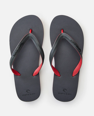 The Rip Curl MC 2 Tone Thongs, featuring black straps with red accents and a thermo rubber compound for comfort, prominently display the brand name on straps and soles. Presented on a sleek white background, they capture attention with their stylish details.