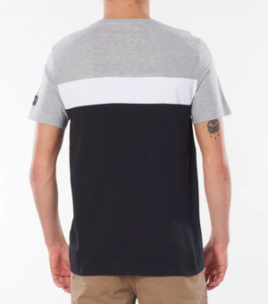 A person wearing a Rip Curl Undertow Panel Tee with gray, white, and black color blocking and beige shorts stands against a plain white background. Their tattooed left arm adds flair as they face away from the camera.