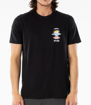The individual models a black Rip Curl Search Icon Tee, crafted from organic cotton. It features a vibrant abstract design of orange, yellow, and pink waves beneath a sun, set against a plain white backdrop.