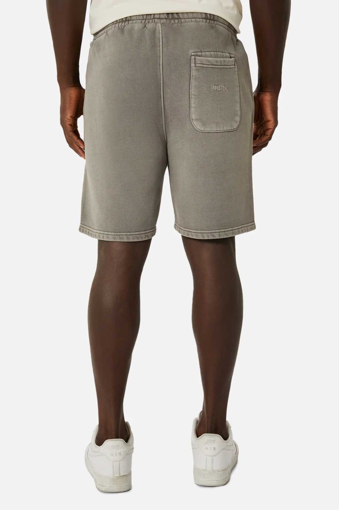 Wearing Industrie The Del Sur Track Short in light gray with an oversized fit and elastic waist, a person stands with their back to the camera. The track shorts have one visible back pocket on the right side, paired with white sneakers against a plain white background.