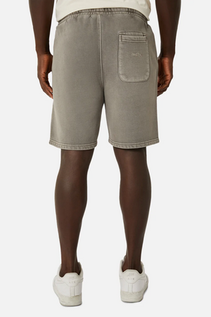 Wearing Industrie The Del Sur Track Short in light gray with an oversized fit and elastic waist, a person stands with their back to the camera. The track shorts have one visible back pocket on the right side, paired with white sneakers against a plain white background.