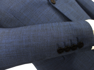 Close-up of the sleeve from a Scuzzatti Slim Fit Suit jacket in blue, displaying a textured fabric with a subtle pattern. The sleeve features four black buttons near the cuff. Check our size guide for accurate half chest measurements and fit details.
