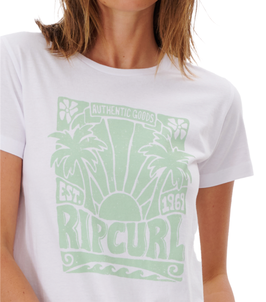 A person is partly visible from shoulders to chin, wearing a Rip Curl Sol Seeker Standard Tee in white organic cotton with a light green graphic design of palm trees, a sun, waves, and the words "Authentic Goods Est. 1969 Rip Curl.