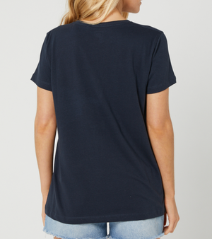 A woman with long blonde hair is seen from the back, wearing a Rip Curl Beachside Standard Tee in navy and light blue denim shorts against a plain white background.