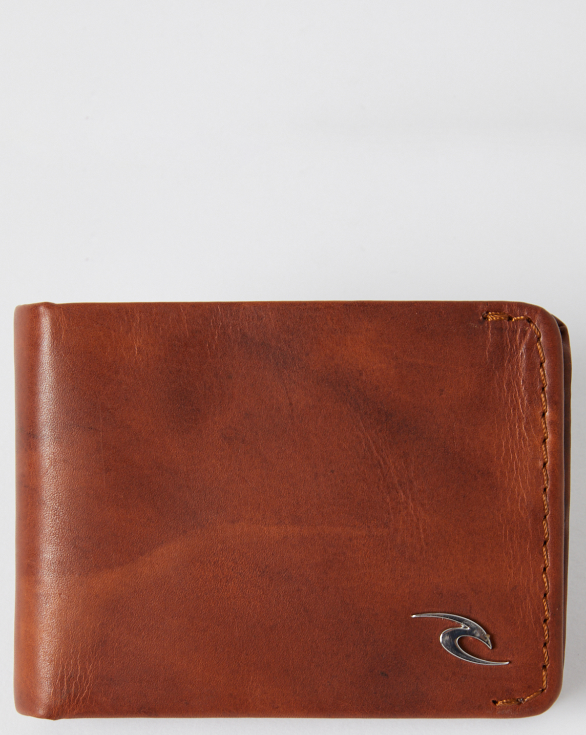The Rip Curl Corpo RFID Slim Wallet, crafted from brown nubuck leather with visible stitching, rests on a plain white background. It features a small metallic logo elegantly integrated into the bottom right corner, combining modern functionality with sophistication.