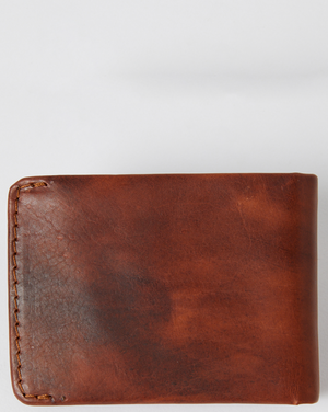 The Rip Curl Corpo RFID Slim Wallet is crafted from brown nubuck leather with visible edge stitching, set against a plain gray background. Its surface features a slightly weathered texture, enhancing its character.
