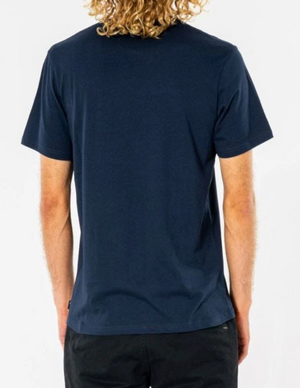 A person with curly blonde hair is wearing a navy blue Rip Curl Big Mumma Icon Tee and black pants, shown from the back against a plain white background.