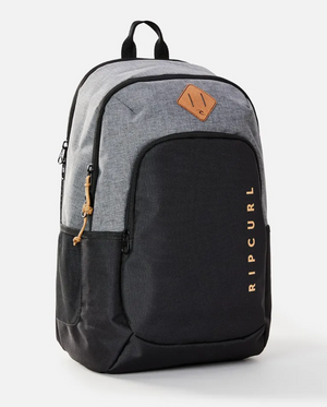The Rip Curl Ozone 30L Driven Backpack, crafted from sleek gray and black polyester, features a front pocket, small leather patch, vibrant orange brand lettering on the side, top handle, and sturdy zippers for both style and functionality.