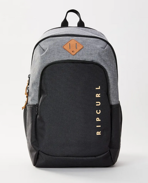 The Rip Curl Ozone 30L Driven Backpack features a stylish two-tone gray and black design. Made from durable polyester, it includes a front pocket with "RIP CURL" in gold, a leather logo patch, side pockets, and a convenient top handle for carrying.