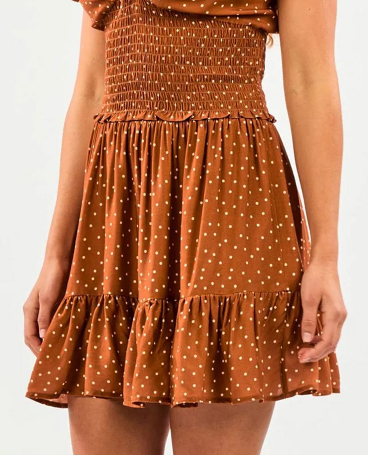 Someone is wearing a brown Rip Curl Dreamer Spot Mini Skirt with white polka dots, featuring a smocked waist and a ruffled hem, perfectly complementing the plain white background.