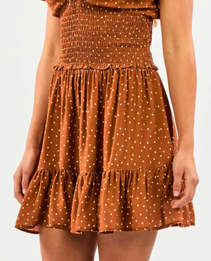 Someone is wearing a brown Rip Curl Dreamer Spot Mini Skirt with white polka dots, featuring a smocked waist and a ruffled hem, perfectly complementing the plain white background.